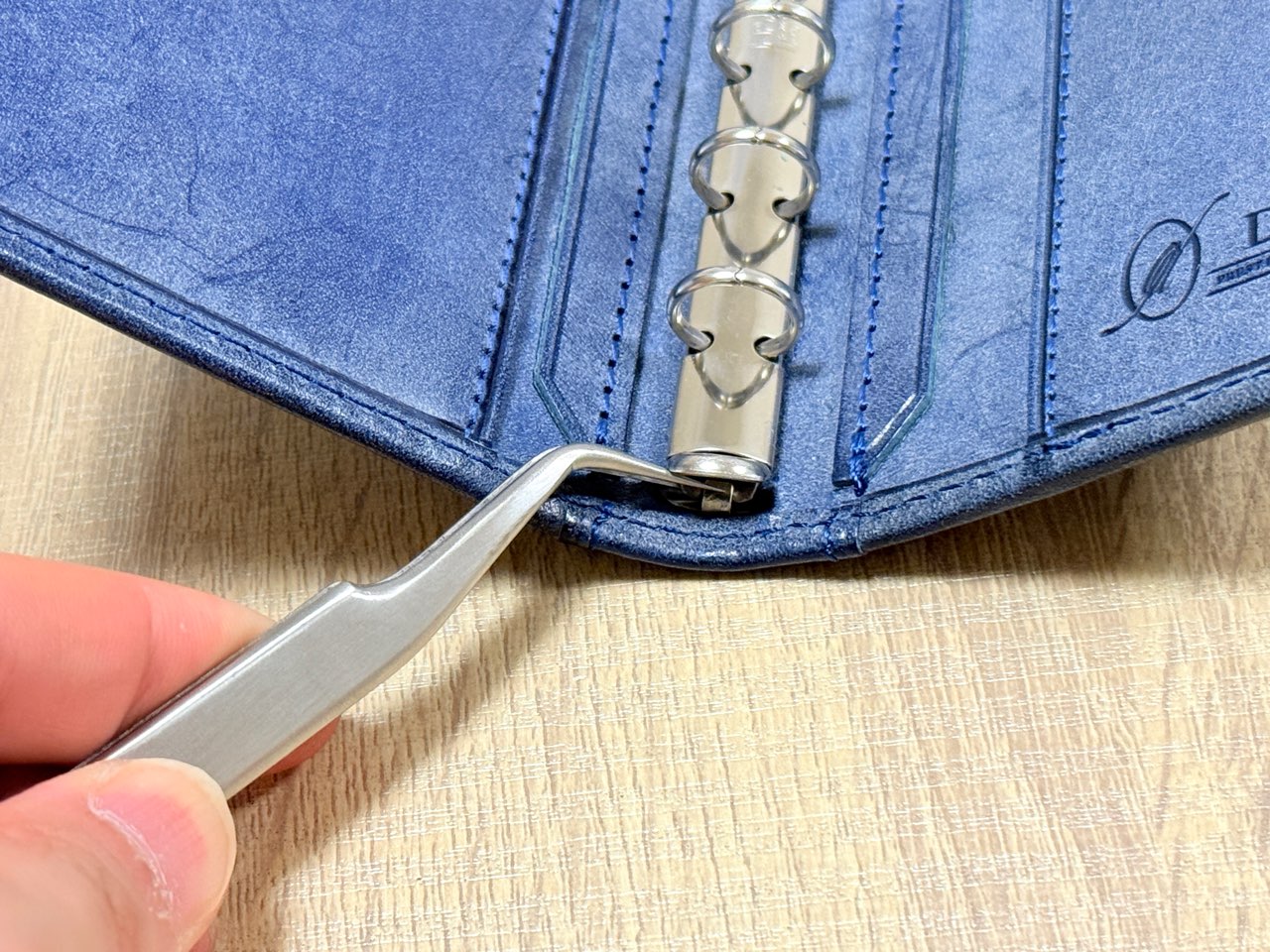 ピンセットでリングバインダーの爪を外そうとしているシステム手帳